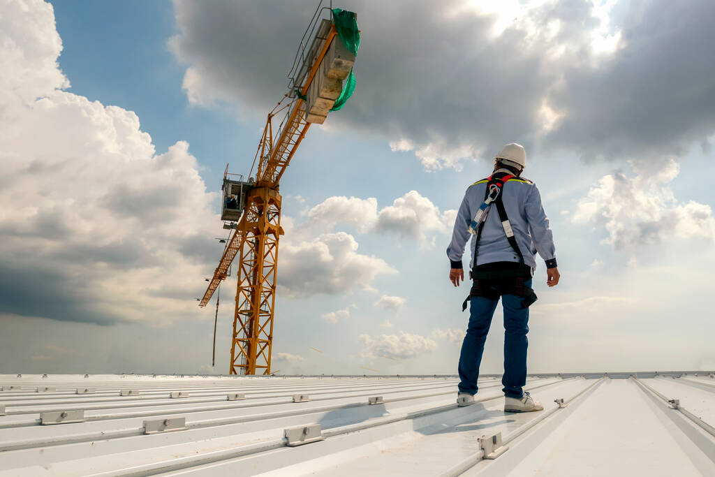 Construction worker on a roof looking at a crane